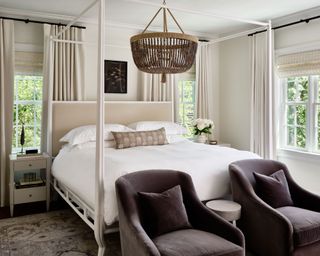 Cream and beige bedroom, beaded chandelier, modern four-poster bed, two armchairs at foot of bed