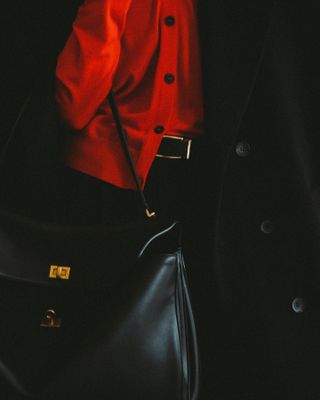 Neelam Ahooja in a black coat, red shirt, and black Balenciaga Rodeo bag.