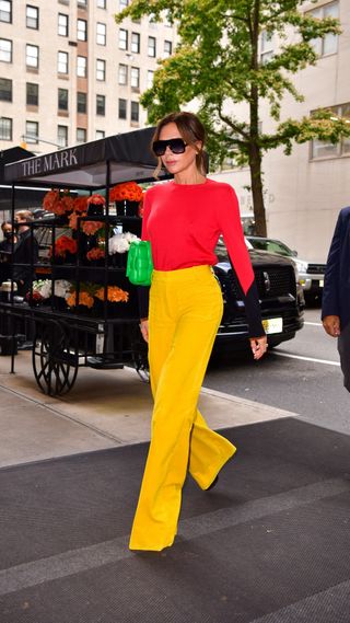 Victoria Beckham in a red top and yellow wide-leg trousers