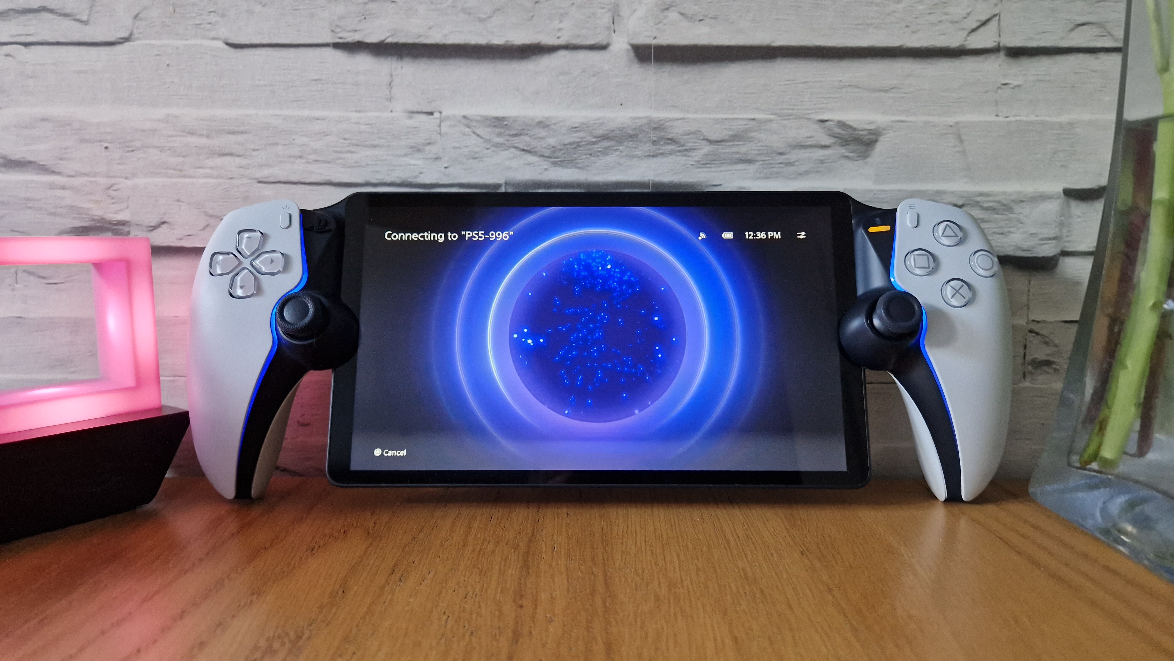 En PlayStation Portal på et skrivebord, lent mot en hvit murvegg.