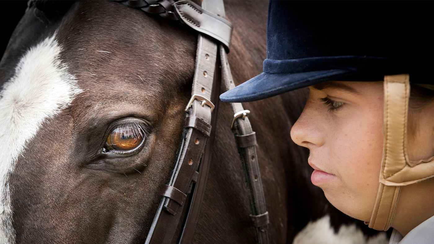 Girl wearing velvet riding hat up close with her horse&amp;rsquo;s head
