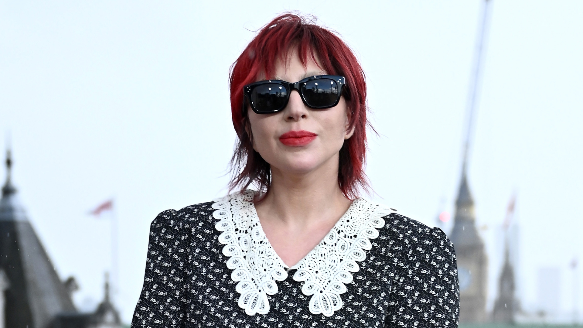 A woman with red hair wearing black sunglasses and a black and white shirt
