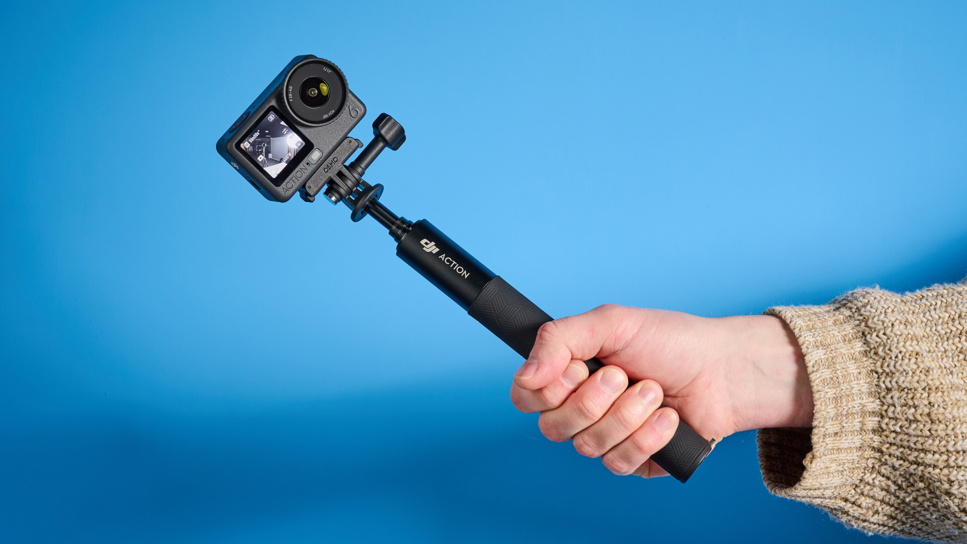 The DJI Osmo Action 6 in hand on a selfie stick with a blue background