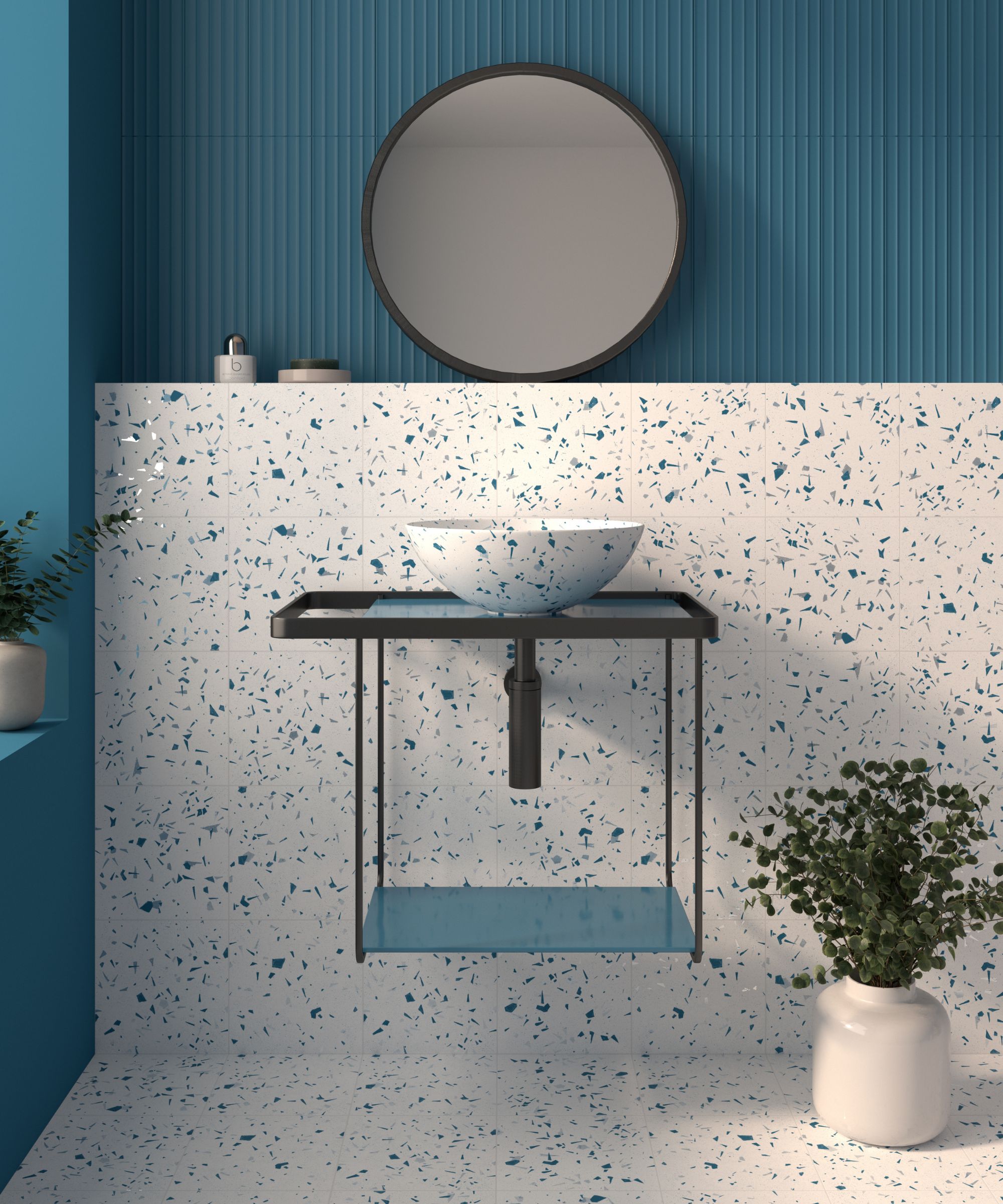 A bathroom with blue and white terrazzo-effect wall and floor tiles, a round black-framed mirror, open metal vanity unit and matching terrazzo basin.