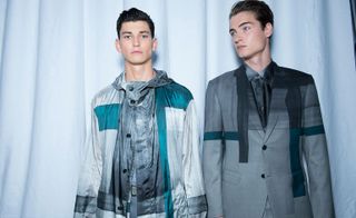 Two models wearing Brioni fashion, one wearing grey suit and one wearing light grey casual jacket both with turquoise accents