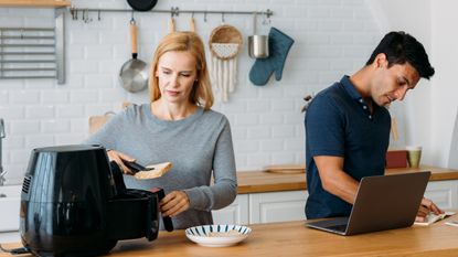 Woman working with airfryer and man using laptop