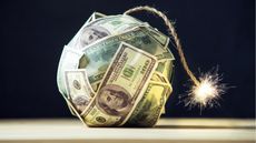 A ball made of cash is attached to a lit fuse.