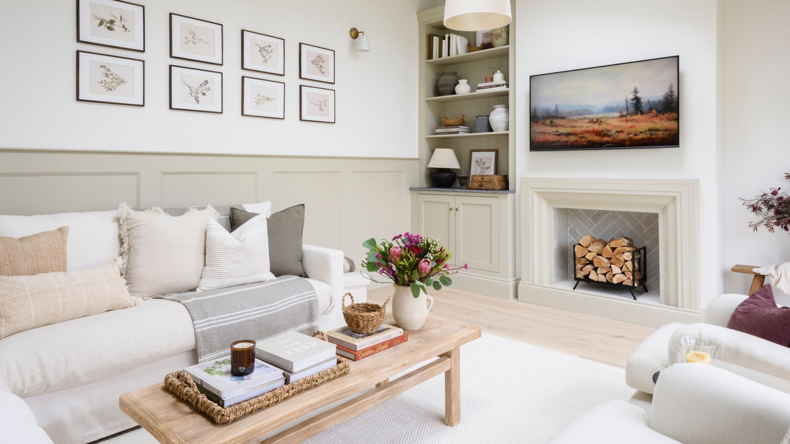 White painted living room with beige panelling on the bottom of the wall and a recessed fireplace area. There's a white sofa covered in cushions 