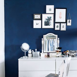 Blue bedroom with white dressing table and framed prints