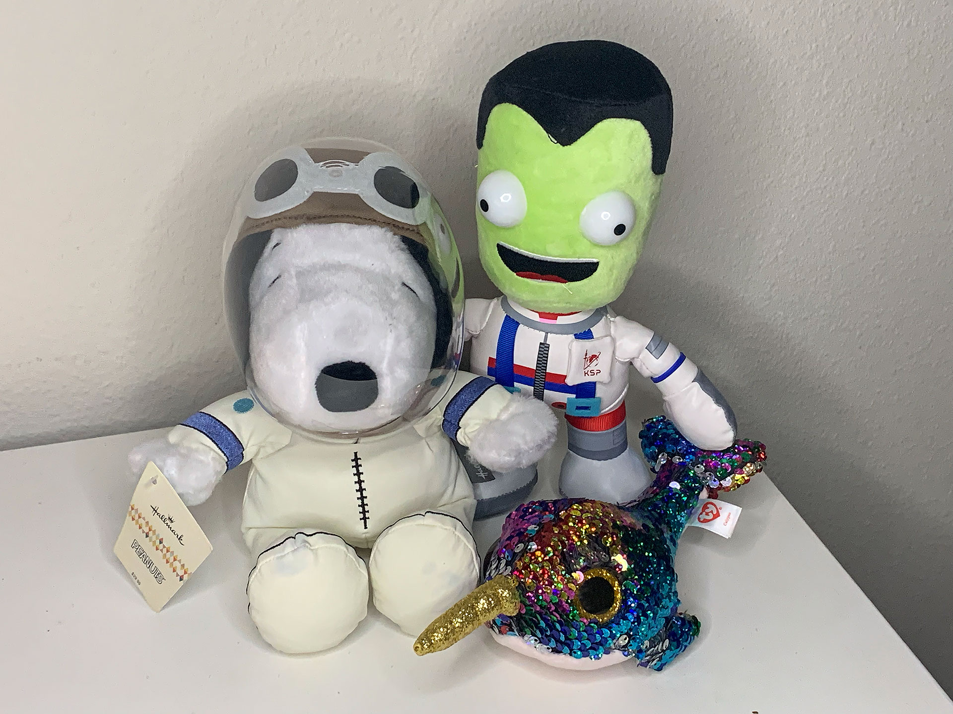 photo of two small plush toys wearing spacesuits — one a white dog and the other a green-skinned humanoid