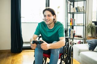 A man in a wheelchair is using a game controller to play a game on the playstation.