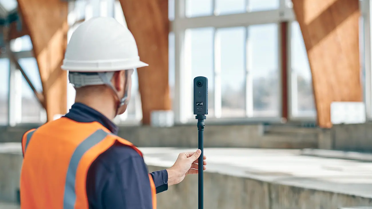 Ricoh Theta A1 360 camera mounted to a monopod, handled by a worker on a construction site