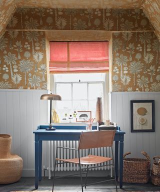 Home office with blue desk and chair, wood paneled walls in white, and neutral patterned wallpaper