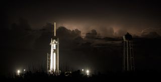 Lightning illuminates the night sky behind the water tower at Launch Complex 39A on May 29, 2020, as SpaceX's Falcon 9 rocket and Crew Dragon stand ready for a second launch attempt, scheduling for the following day.