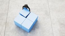 Arial view of a man rearranging four big blue blocks.