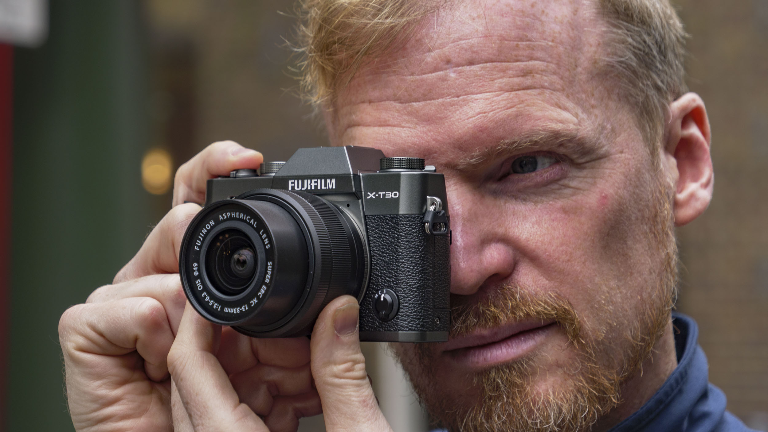 Man holding the Fujifilm X-T30 III camera up to his eye, on London street
