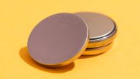 High angle view of three used CR2032 lithium button cell batteries isolated on yellow background