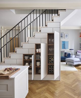 An under stairs idea with three tall white cabinets built into kitchen staircase