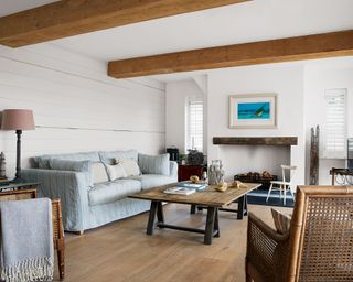 A white living room with wooden beams, wooden coffee table, woven chairs and a pale blue sofa.