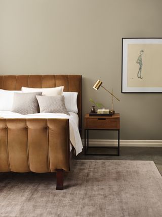 bedroom with stone walls, upholstered bed, side table, taupe rug, artwork, brass table lamp