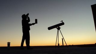 Sylwetka dwóch osób i ich teleskop są nakreślone na świecącym nocnym niebie