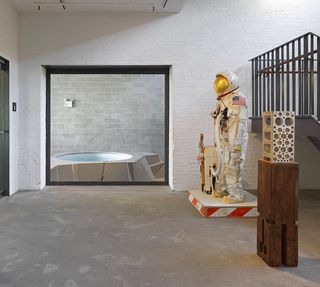 Exhibition by Tom Sachs with space suit, pool and metal block on a wooden podium
