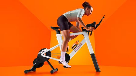 A women riding a Zwift smart trainer with an orange background