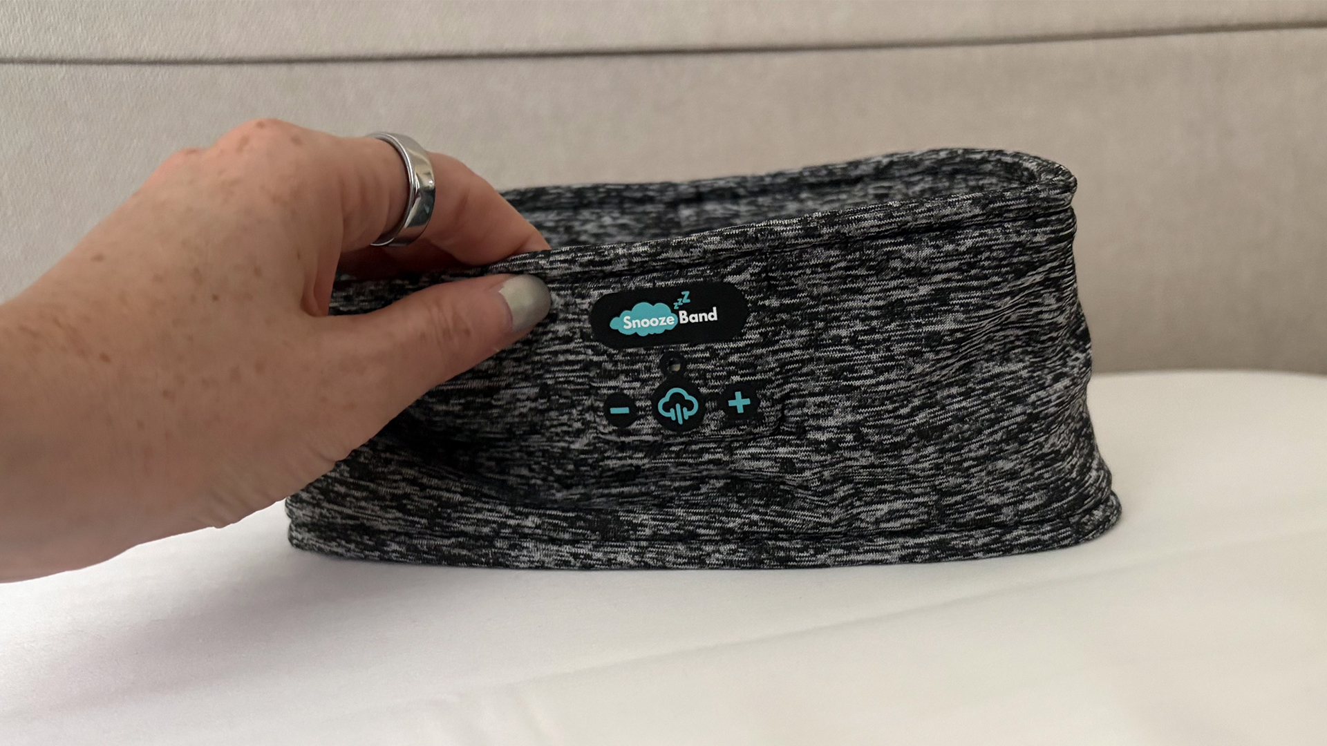 A hand reaches out to touch the SnoozeBand Original Sleep headphone, balancing on a pillow in our reviewer's bedroom