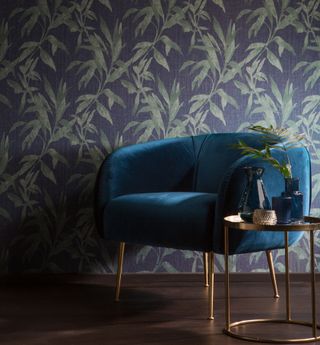 dark toned botanicla wallpaper in blue with green accompanied by blue velvet chair and side table. wallpaper by galerie wallcoverings