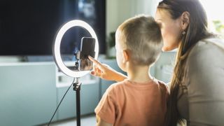 Mother live streaming with son on smart phone with ring light at home