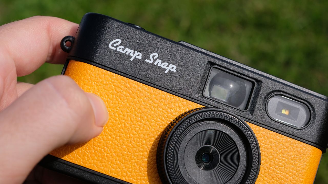 Photograph of man's hand holding Camp Snap 2 digital camera, in yellow colorway