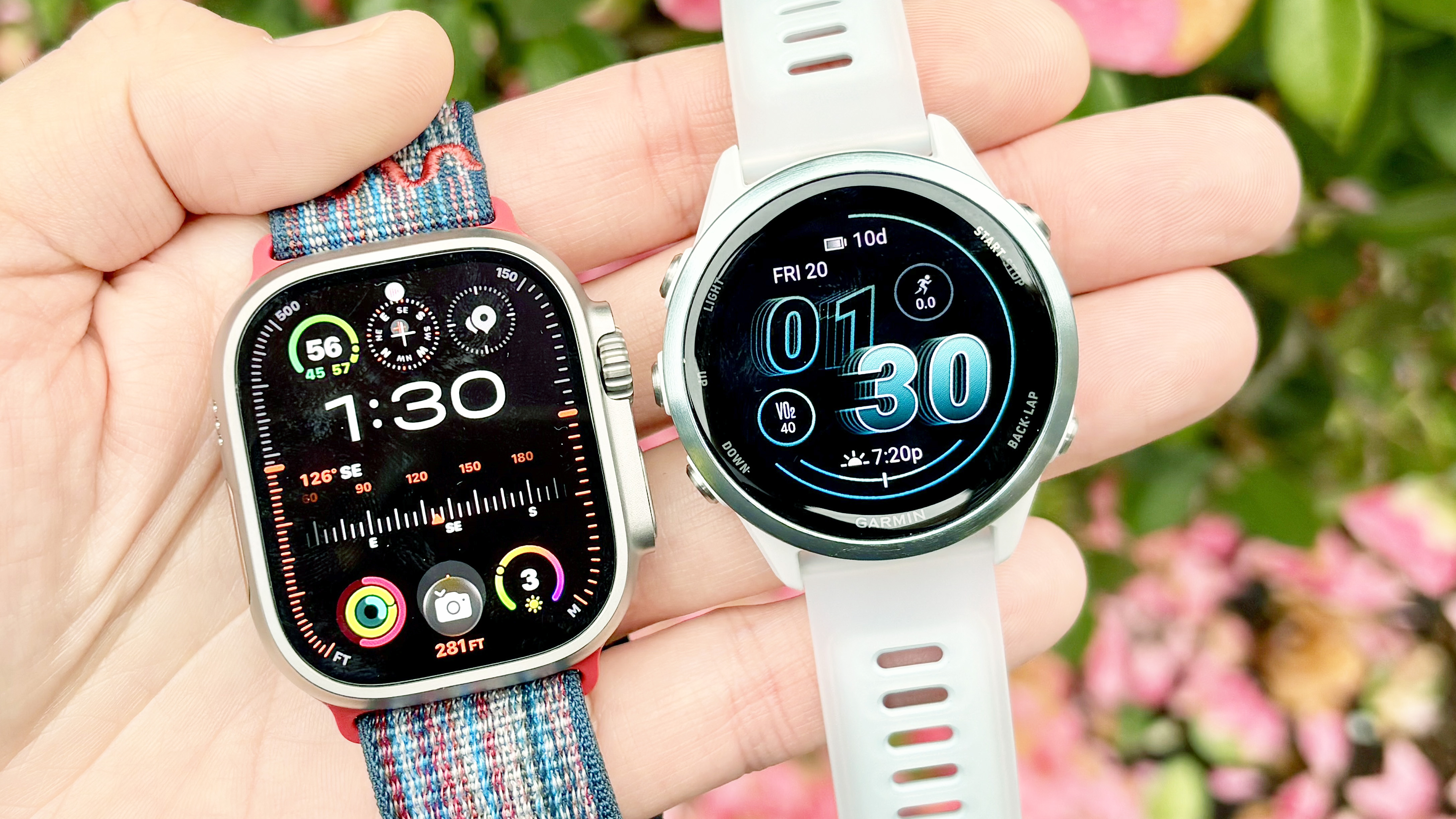 Close-up of the Apple Watch Ultra 3 and Garmin Forerunner 570 in a user's hand with blooming flowers in the background