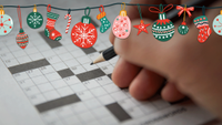 A hand holding a pencil over a crossword puzzle with christmas decorations layered over the top