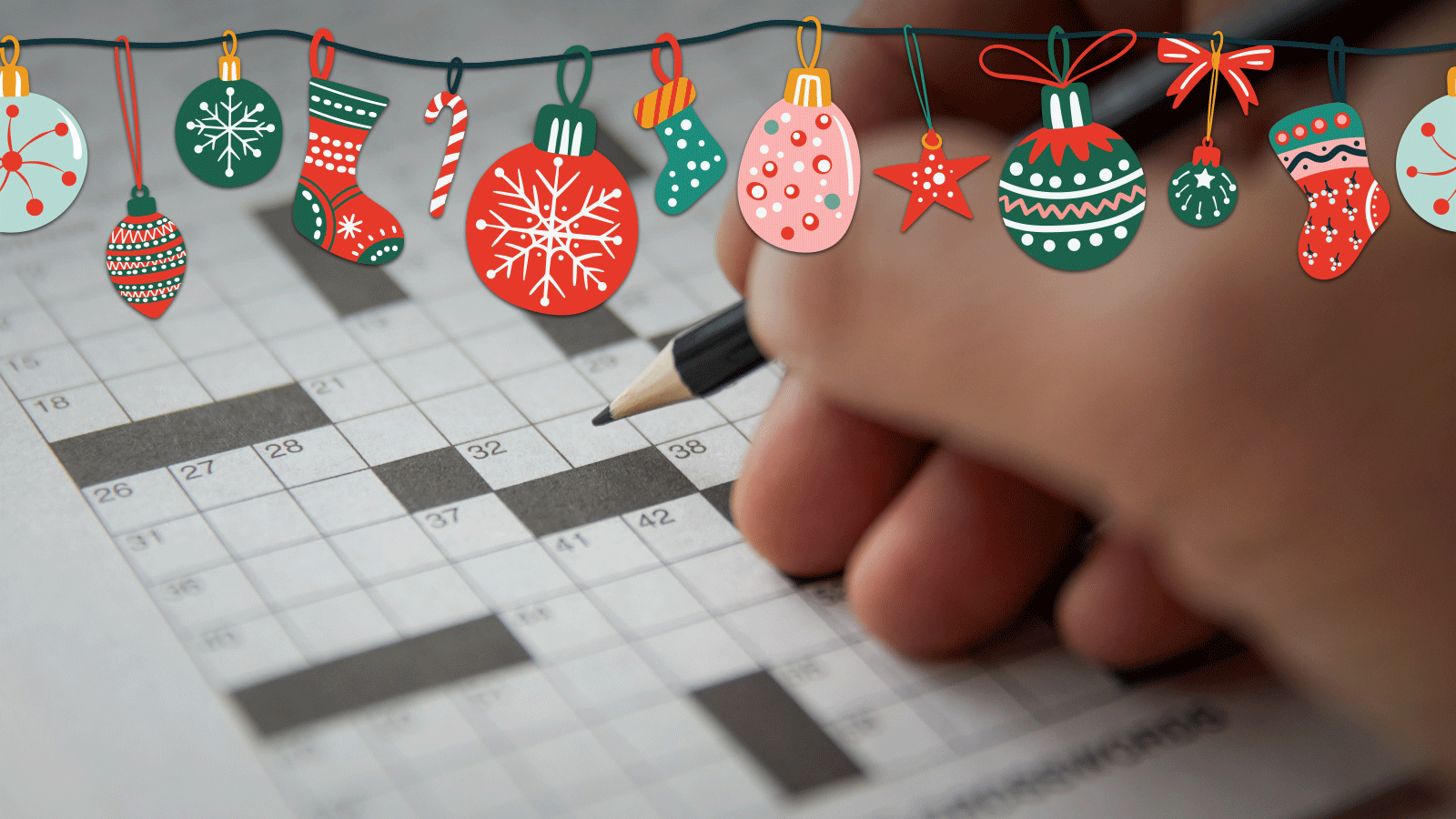 A hand holding a pencil over a crossword puzzle with christmas decorations layered over the top