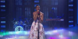 Kid Cudi wearing a white floral dress in a tribute to Kurt Cobain while singing into a microphone on SNL.