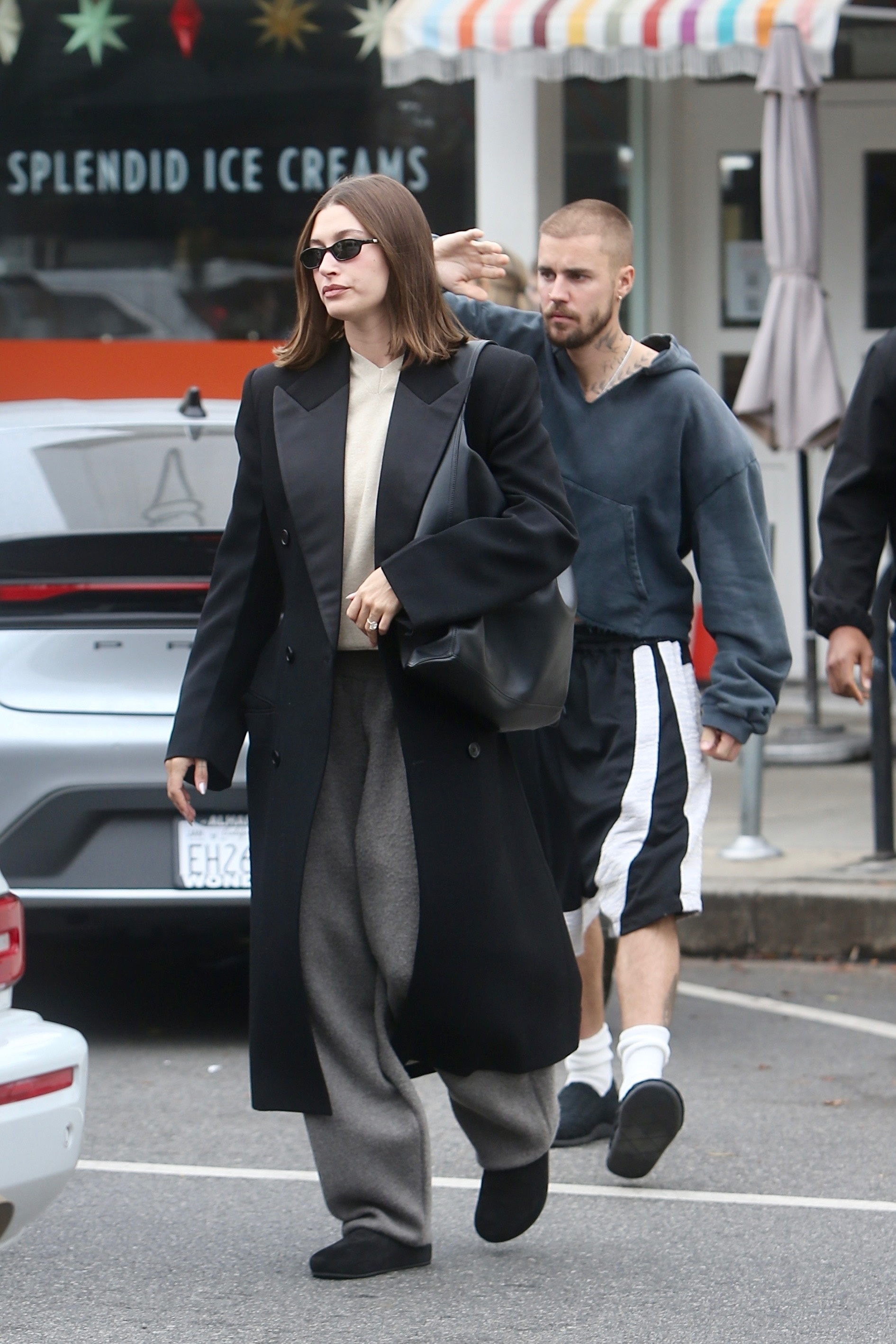 Hailey Bieber wears gray sweatpants and black slippers with a long winter coat and carries a black leather oversize bag as she grabs lunch with husband Justin Bieber
