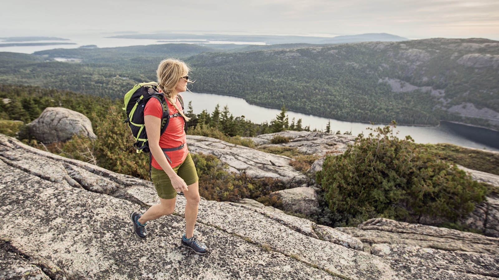An active woman takes in in the view of the Atlantic Ocean from the summit of Pemetic Mountain while hiking in Maine&#039;s Acadia National Park.