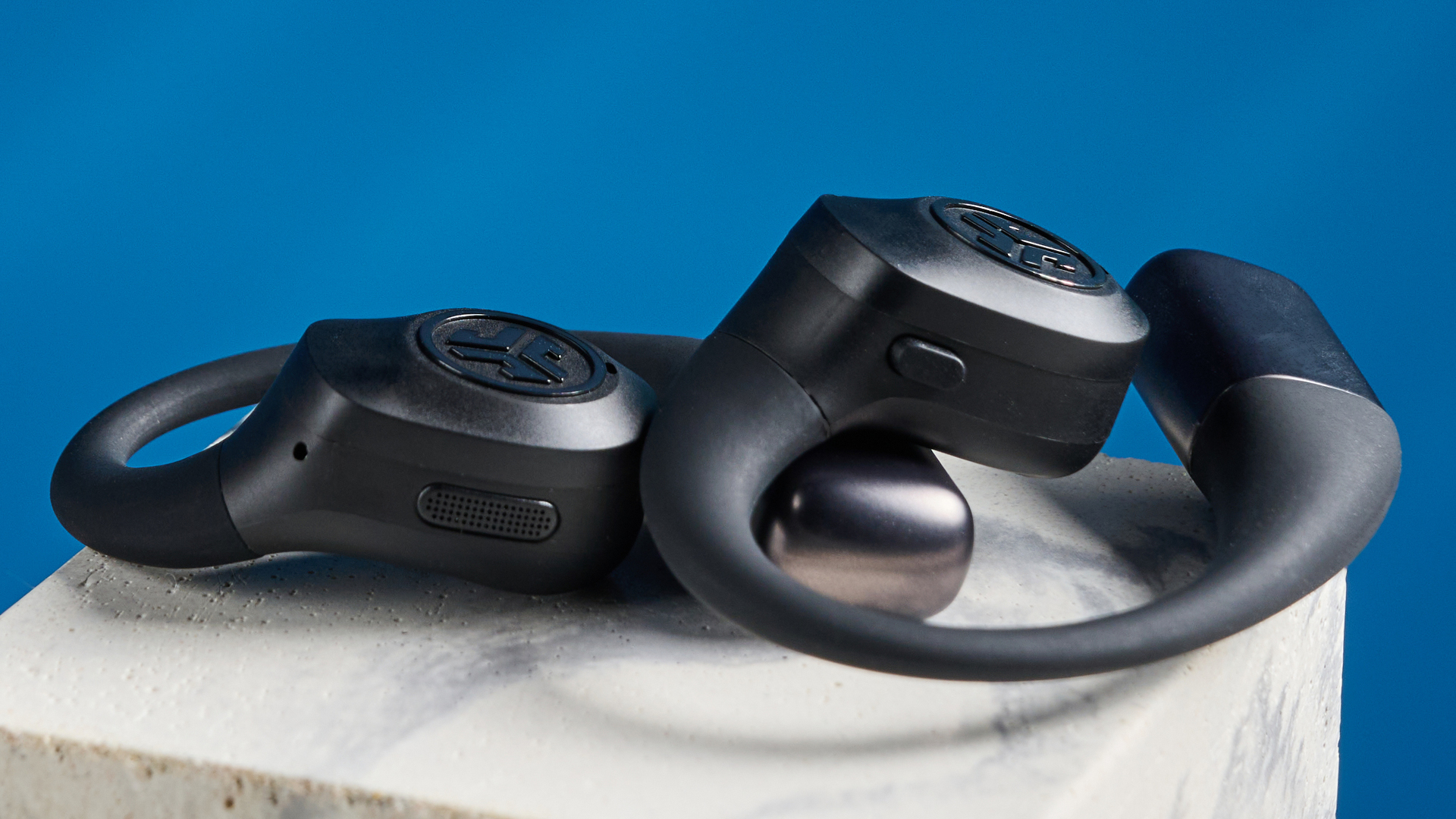 Jlab epic open sport open-earbuds in a black colorway photographed on a blue background.
