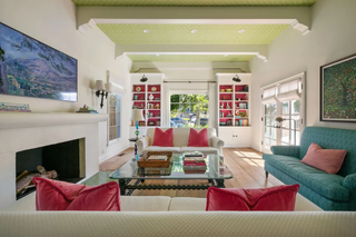 A living room with a green ceiling, a blue sofa, and pink accent cushions and pink painted bookshelves