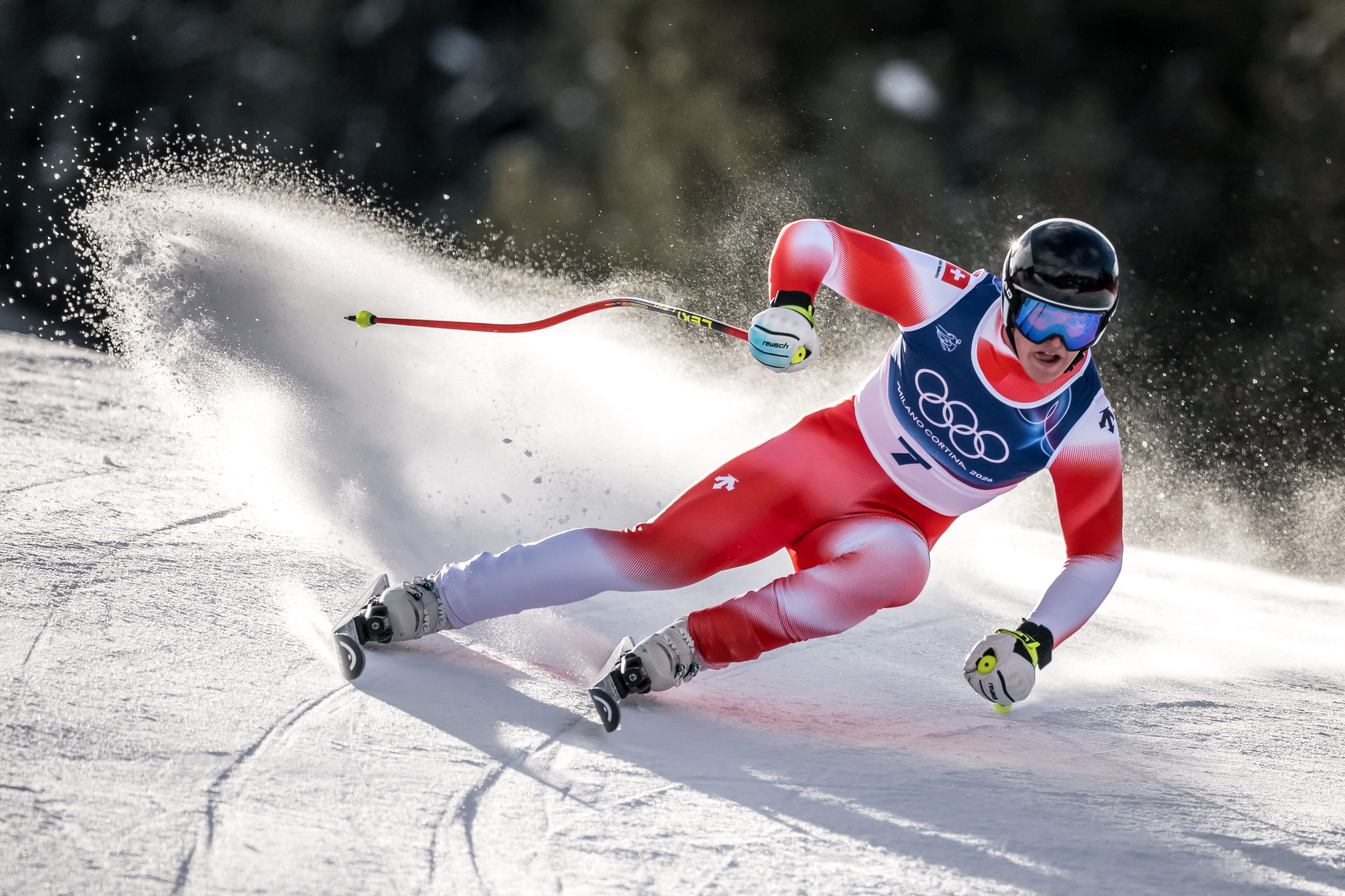 A Swiss skier on a sunny slope making a turn with snow being kicked up
