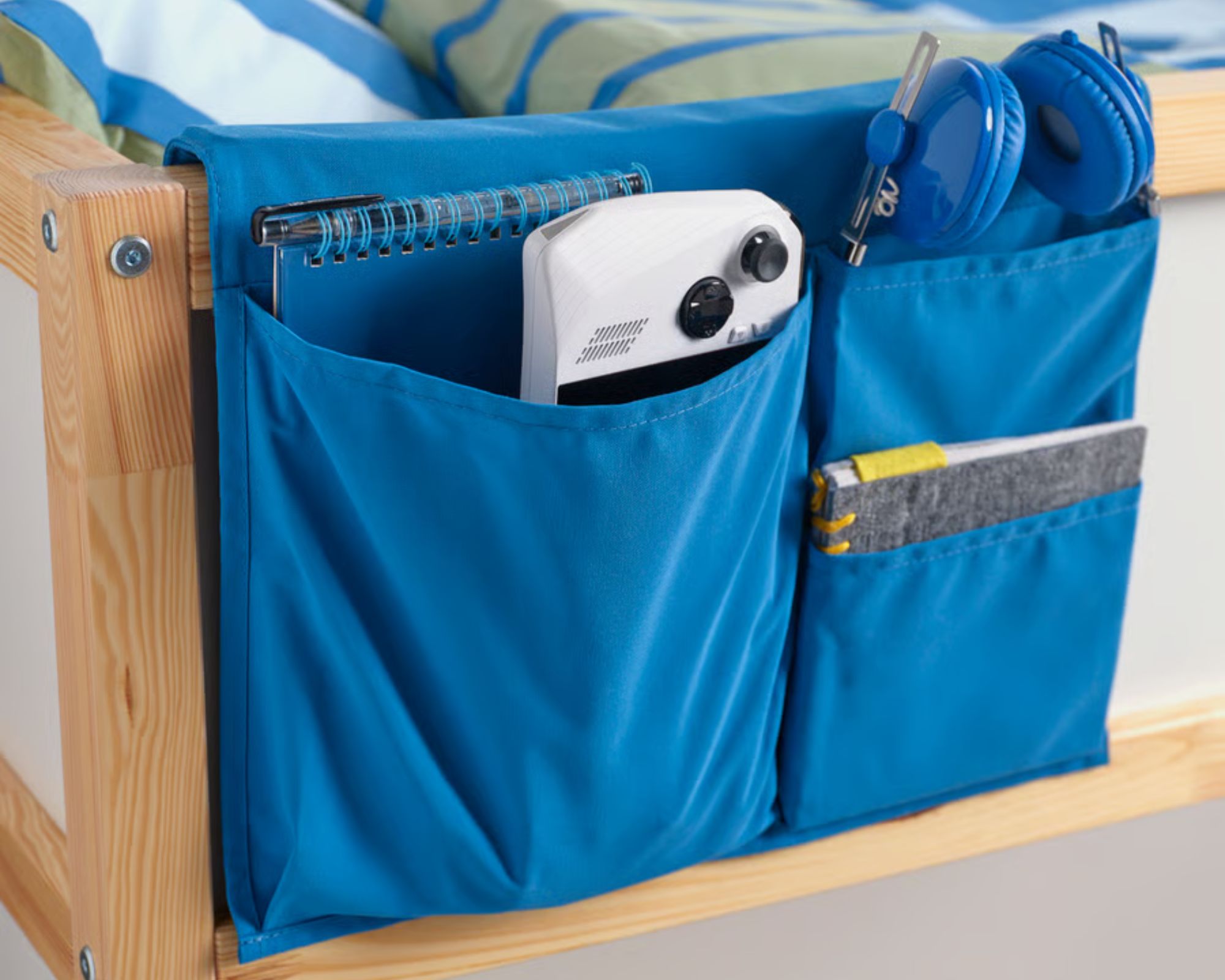 Blue IKEA Stickat Bed Pocket on a light wood bedframe with blue and green bedding.