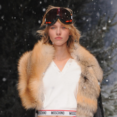 model walks down the catwalk with fake snow wearing a fur coat and ski goggles - Skiing skincare routine