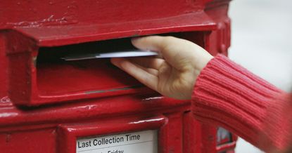 A hand placing a letter inside a Royal Mail post box