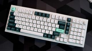 A Keychron Q5 HE gaming keyboard on a desk with white and blue keycaps.