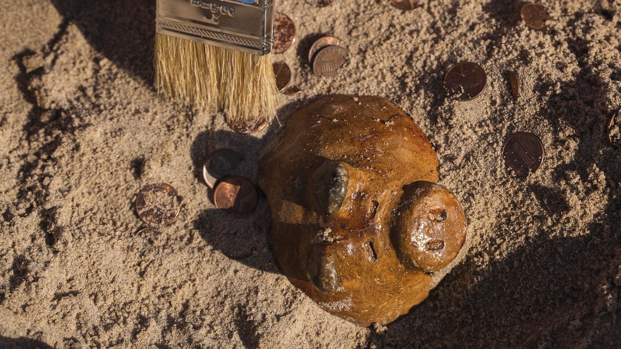 An aged piggy bank appears to be excavated from sand.