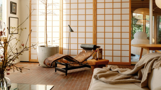 A Japanese living room with sliding screens, vases, a tall potted tree, a cow-print chaise lounger, and a beige sofa