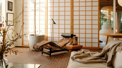 A Japanese living room with sliding screens, vases, a tall potted tree, a cow-print chaise lounger, and a beige sofa