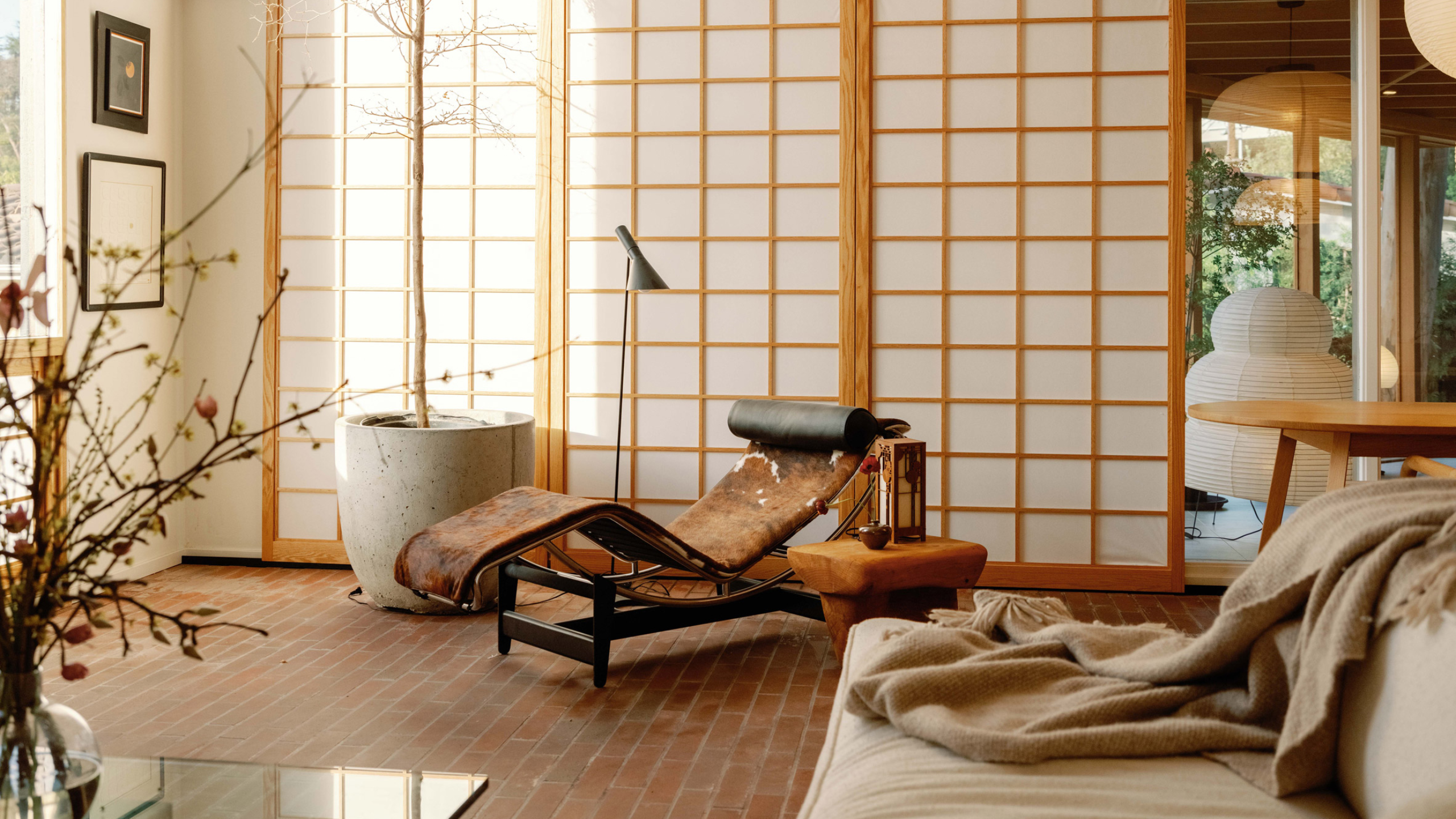 A Japanese living room with sliding screens, vases, a tall potted tree, a cow-print chaise lounger, and a beige sofa