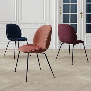Three GamFratesi beetle dining chairs in various colours arranged in a dining room.