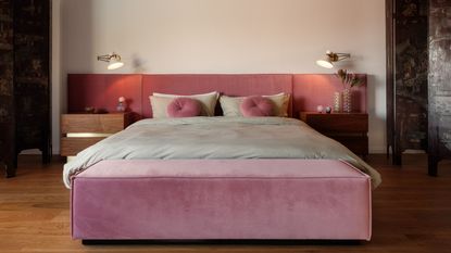 Image of a white bedroom with hardwood flooring, a pink upholstered bed with mint green bedding.